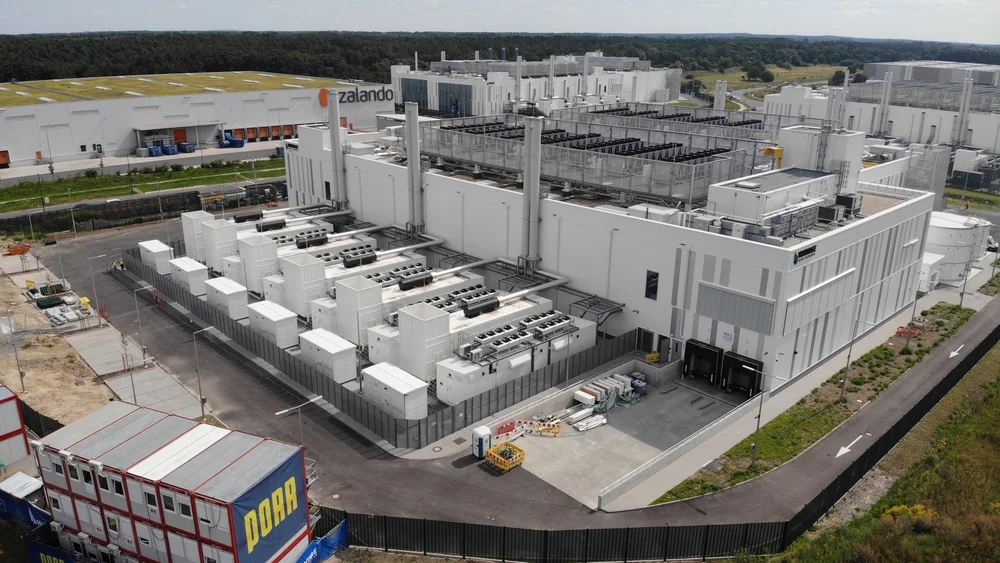 Auf dem Bild sieht man das BER12 Datacenter in Ludwigsfelde bei Berlin. Im Vordergrund stehen mehrere Baucontainer, auf deren Seite das Logo der PORR zu sehen ist.