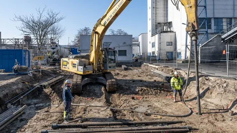 Fertigrammpfähle; Bild zeigt zwei Männer neben einer Maschine mitten auf einem Bauplatz;Die beiden arbeiten an einem Fertigrammpfahl genauer gesagt, einem duktilen Rammpfahl