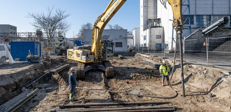 Fertigrammpfähle; Bild zeigt zwei Männer neben einer Maschine mitten auf einem Bauplatz;Die beiden arbeiten an einem Fertigrammpfahl genauer gesagt, einem duktilen Rammpfahl