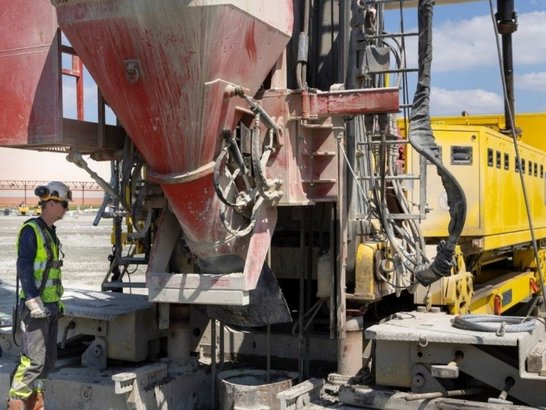 Bild zeigt eine Baustelle. Ein Bauarbeiter steht vor einem großen Baugerät 