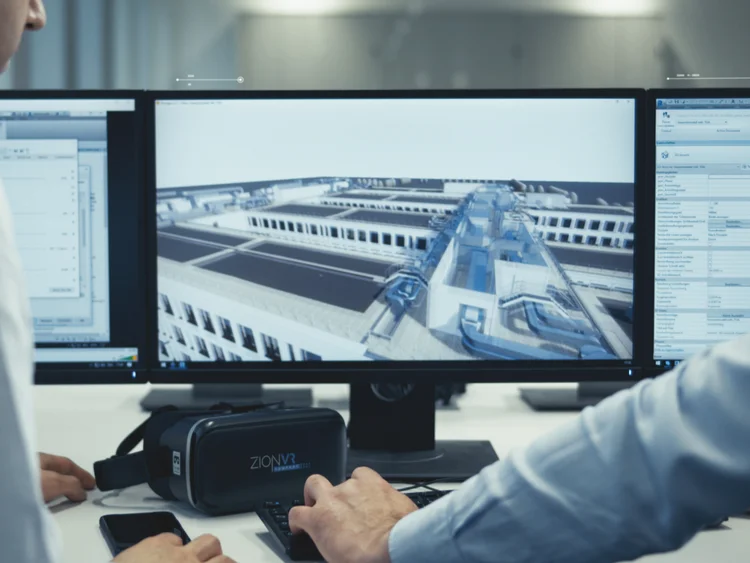 Picture shows 2 men in front of a computer. They are looking at the screen.