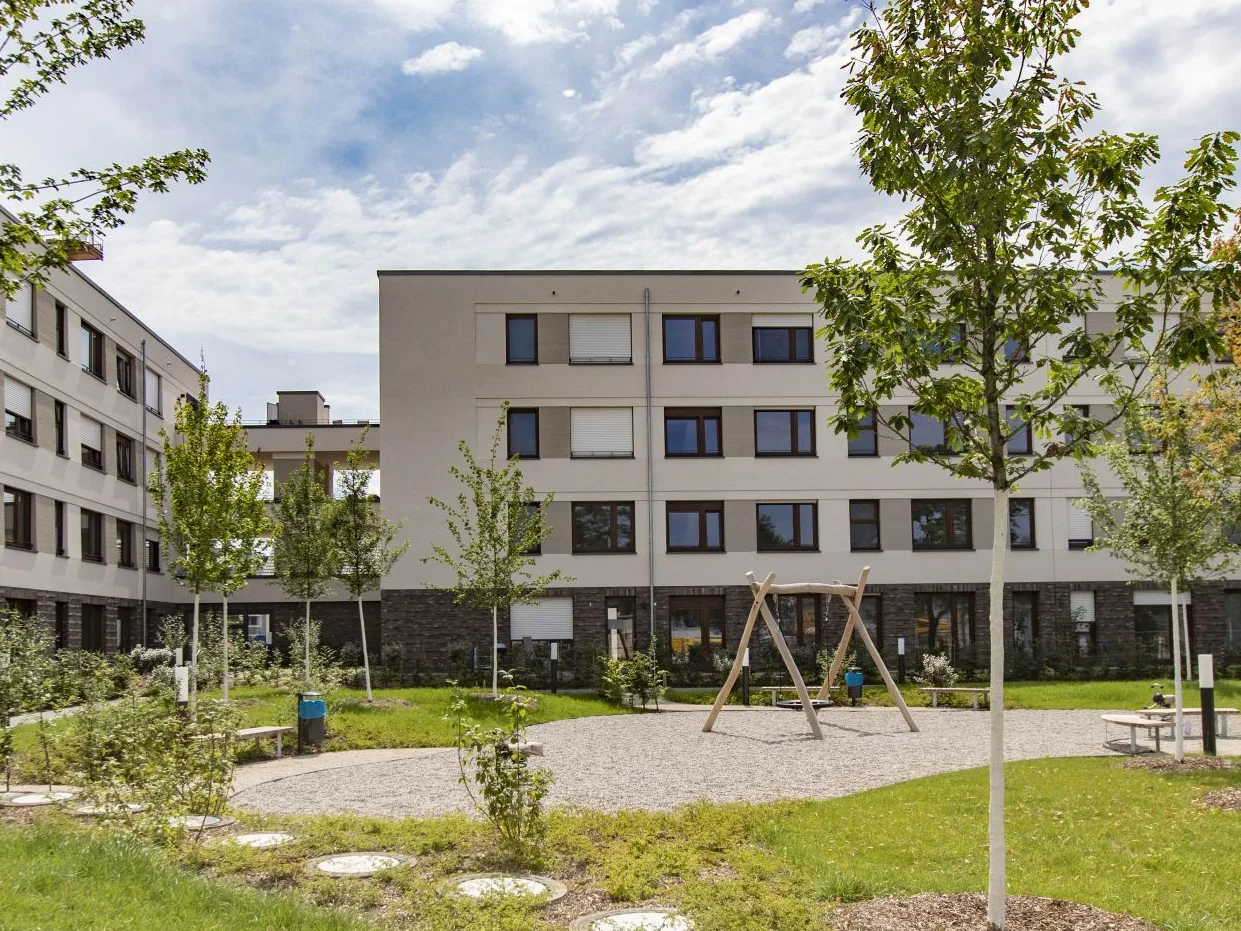 Jackson Three im Franklin Quartier, Mannheim View of the 4-storey building; the façade surfaces between the windows were painted in different shades of beige; in the foreground is a green area with a small playground and seating;