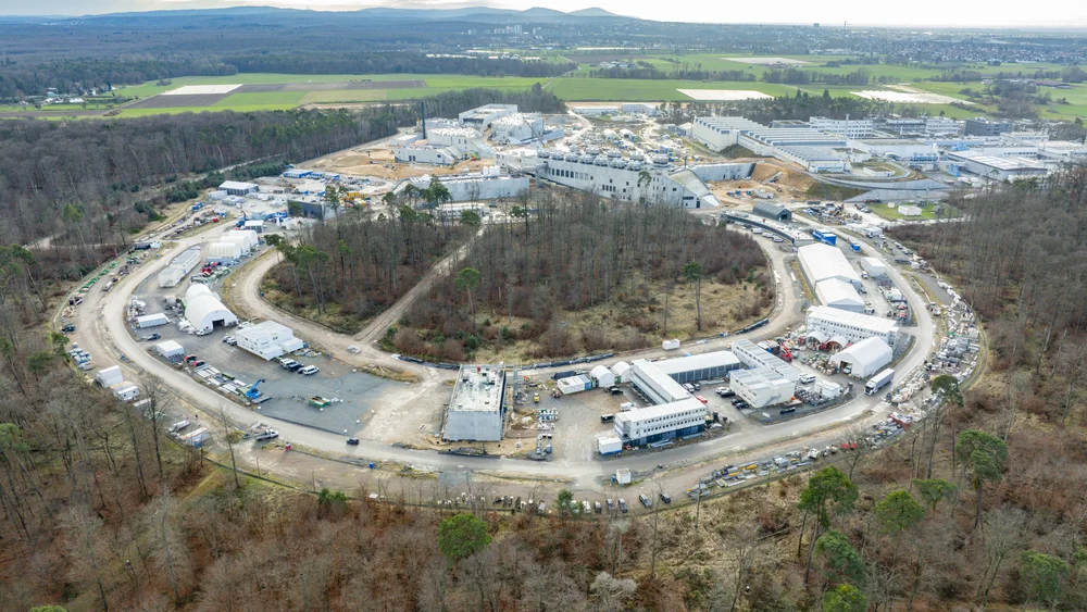 Das Bild zeigt den kreisförmigen Beschleunigertunnel aus der Perspektive einer Drohne. Um den Ring herum wächst ein Wald.