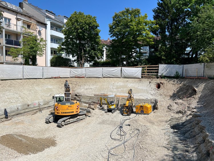 Baugrube des Wohnbauprojekts Pfitznerstraße in München mit Baggern, Bohrgerät und gesicherten Böschungen während der laufenden Erd- und Spezialtiefbauarbeiten.