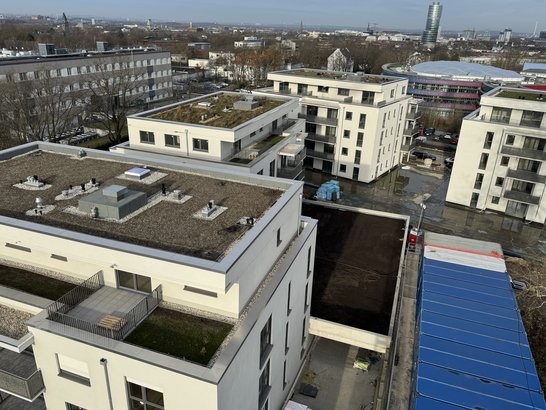 Moderne Neubausiedlung mit Mehrfamilienhäusern, begrünten Flachdächern und Baustellenbereich, Blick über das Wohnquartier bis zur umliegenden Stadt.