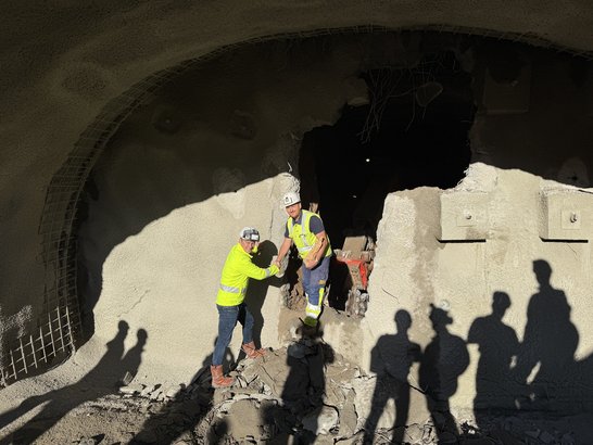 Two construction workers shake hands in front of a freshly excavated tunnel section – symbolizing a successful breakthrough in tunnel construction.