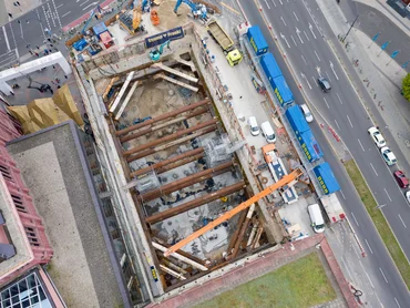 Bild zeigt eine Baugrube von oben. Man sieht rechts die Straße und links ein Gebäude;