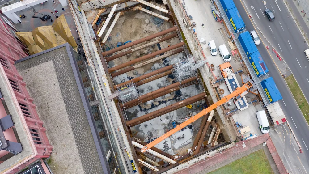 Bild zeigt eine Baugrube von oben. Man sieht rechts die Straße und links ein Gebäude;