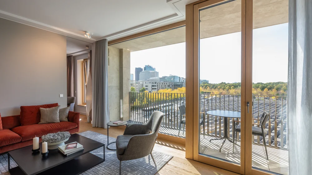 Blick in eine Wohnung; man sieht das Wohnzimmer mit einer Sitzecke; durch die Glasfassade sieht man das Holocaust Mahnmal