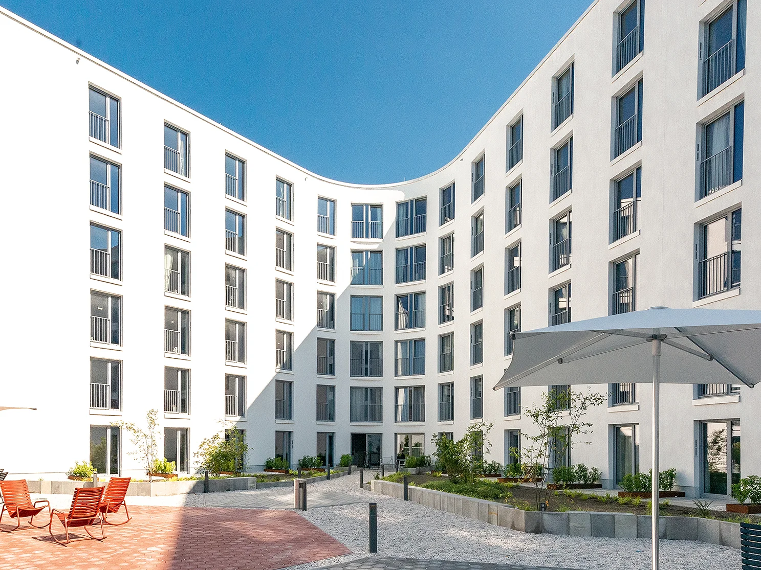 The Fizz -Stresemannquartier, Hamburg The façade with white, floor-to-ceiling windows. In front of this is the inner courtyard with chairs and parasols.