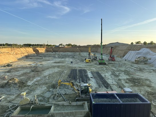 Bild zeigt die Baustelle. Man sieht Baugeräte und die Baugrube.