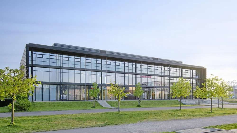 Blick auf die Rückseite des Gebäudes; 3 Grünflächen die durch eine Treppe und Fußgängerwege getrennt werden; man sieht den lichtdurchfluteten, 3-geschossige Erweiterungsbau dieser wurde schlüsselfertigen realisiert Glasfront