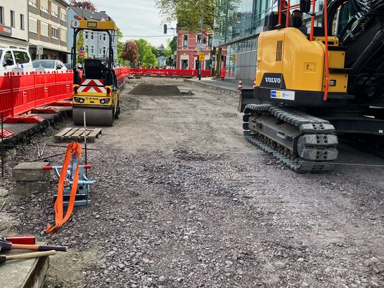 Roadworks in the city centre involving an excavator, a roller and a closed-off carriageway in front of an office building.