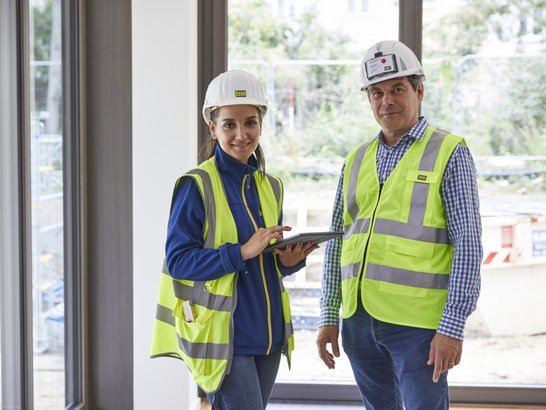 Bild zeigt zwei Bauarbeiter in einem Gebäude. 