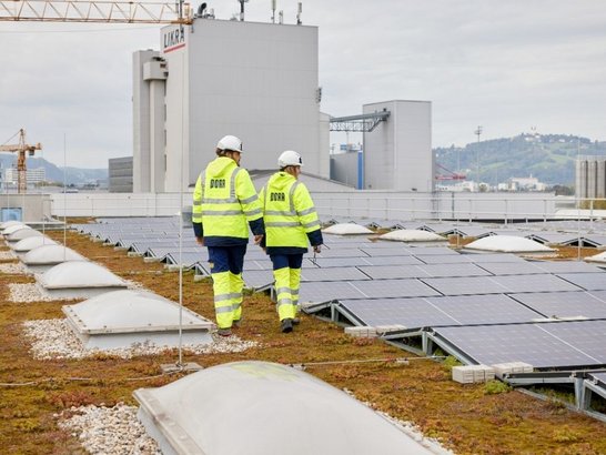 Zwei Bauarbeiter laufen über ein Dach mit Photovoltaikanlagen