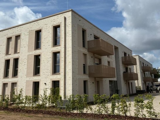 Mehrfamilienhaus Commerhof mit heller Klinkerfassade und Balkonen. Der von PORR realisierte Wohnungsbau zeigt moderne Architektur und großzügige Außenanlagen