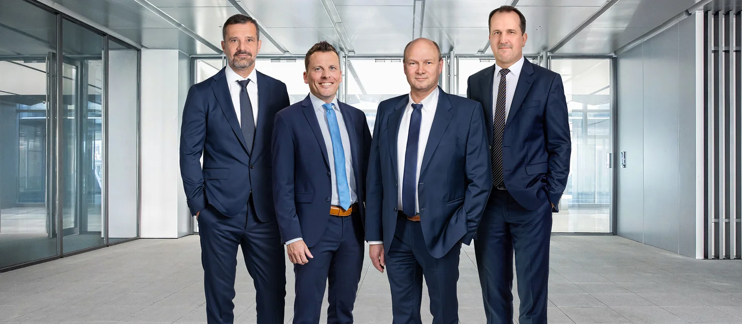 Bild zeigt ein Gruppenfoto der GeschĂ€ftsfĂŒhrung. Man sieht 4 MĂ€nner im Anzug und mit Krawatte.