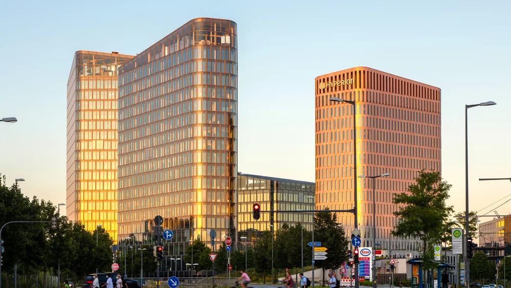 Blick auf die beiden HochhĂ€user des Hotelturms; Links sieht man den Blue Tower der ein BĂŒrogebĂ€ude ist; rechts sieht man ein Hotel, welches zur Marke Hyperion gehört; auffallend ist die raumhohe und bodentiefe Verglasung der Fenster; Bild bei Sonnenaufgang.