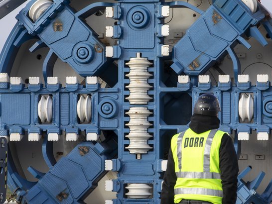 Bild zeigt einen Bauarbeiter, der mit Rücken zur Kamera steht. Er steht vor dem großen Schneiderad der Tunnelbohrmaschine ELSA im Projekt ElbX. 