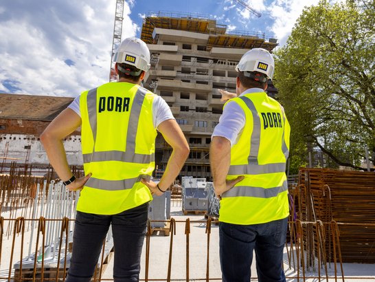 Bild zeigt zwei Bauarbeiter vor einer Baustelle 