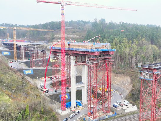 Concrete work on the superstructure of the Horb viaduct: construction of the bridge is progressing on massive piers, supported by cranes, formwork scaffolding and concrete pumps, set against a scenic backdrop.