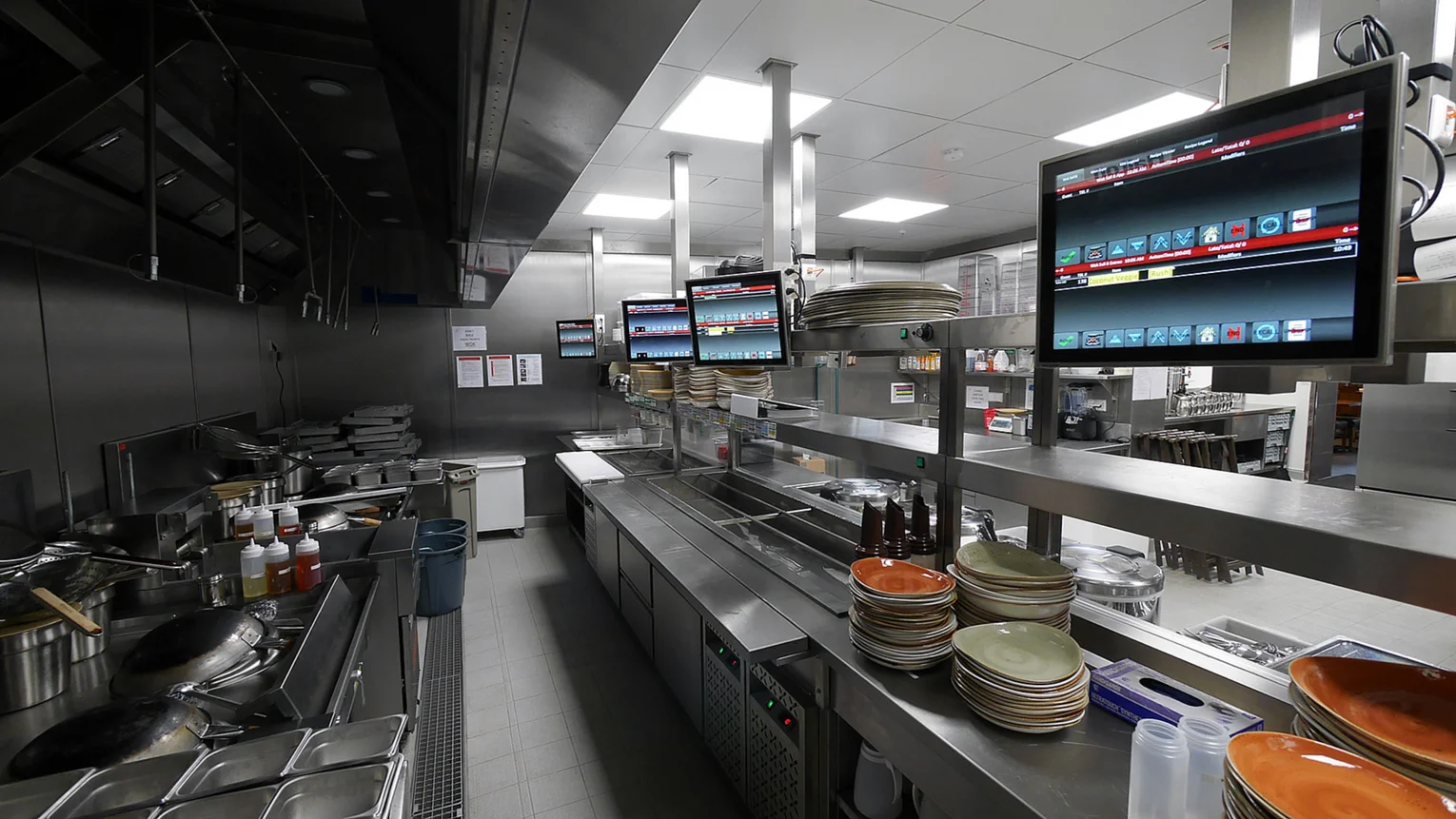 Whipping up American culinary delights. Photo: metal kitchen islands, four screens above them, plates stacked ready for use, wide variety of cooking utensils, extensive lighting