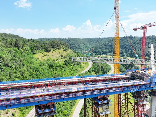 Bild zeigt eine Brücke. Ein Kran bewegt ein Metallteil . 