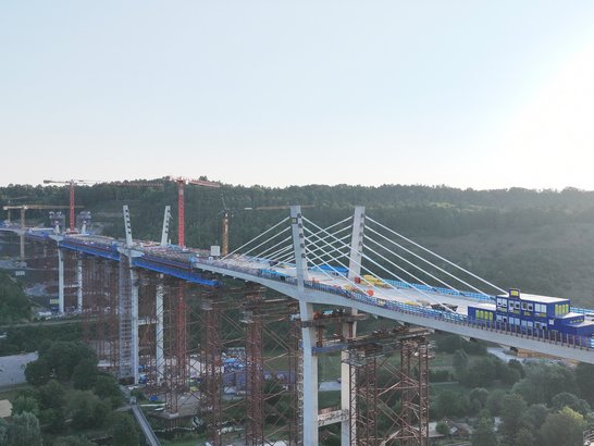 An aerial view of the Horb High Bridge during the construction phase. The cable-stayed structure, several bridge piers and the construction site facilities in the Neckar Valley can be seen.