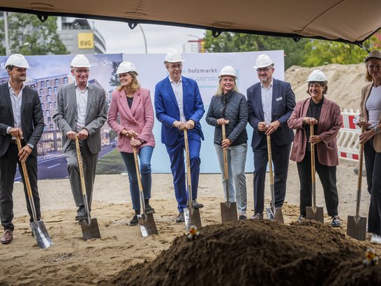 Group photo from the ground-breaking ceremony. People are standing with spades in front of a mound of earth