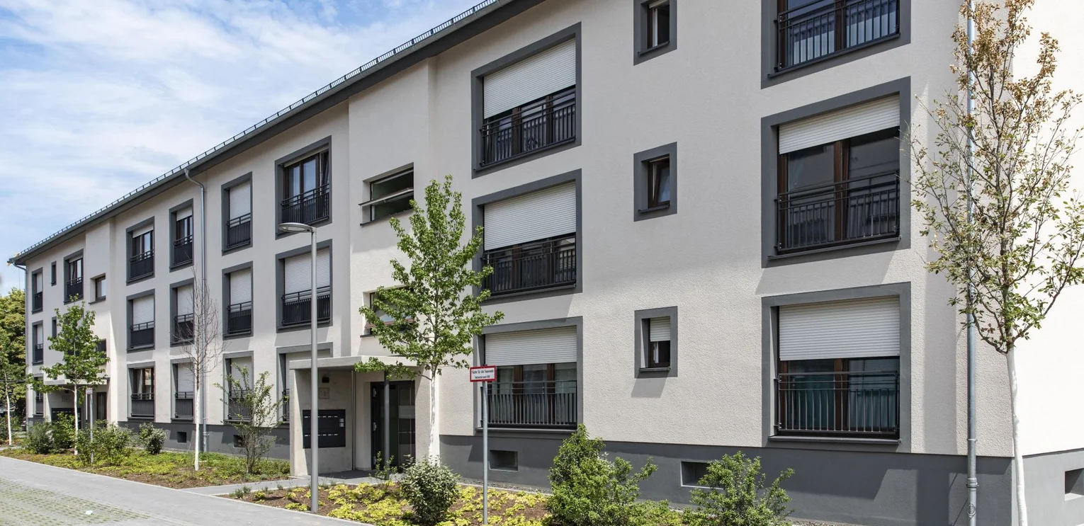 Jackson Three im Franklin Quartier, Mannheim View of the entrance on the street side; beige building complex with floor-to-ceiling windows; the bathroom windows are smaller; all window elements are framed with dark grey paint; the base is also completely dark grey; the entrance is covered;