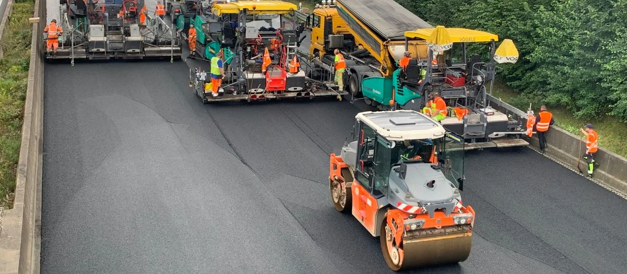 Mehrere Walzen fahren über eine frisch sanierte Straße.