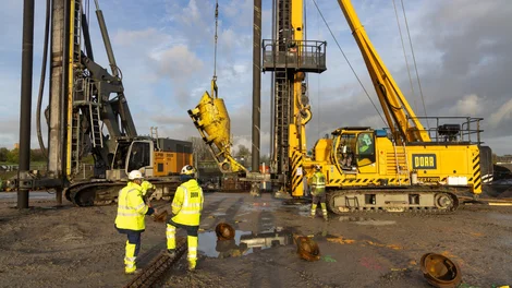 Bild zeigt eine Ramme. Davor steht ein Bauarbeiter.