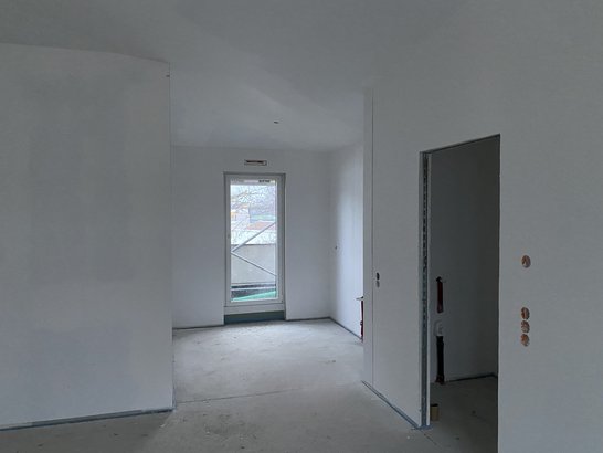 Bild zeigt eine Wohnung beim Innenausbau. Weiße Wände, man sieht den Balkon. 