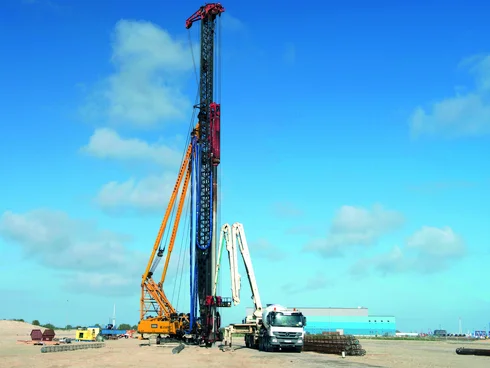 Bild zeigt wie ein Simplexpfahl betoniert wird. Man sieht 2 große Baugeräte. Im Hintergrund zwei Kräne